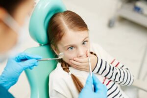 little girl covering her mouth with the dentist holding instruments