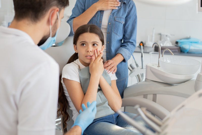 child with a toothache and a concerned parent behind her